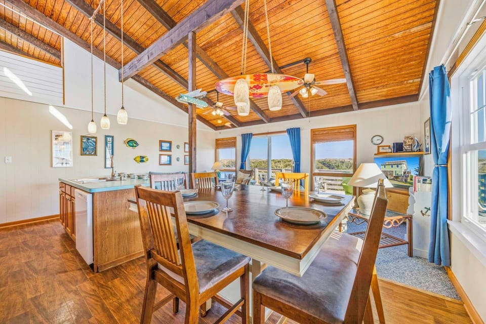 Gather around your rustic dining table beneath soaring wood-beamed ceilings, where coastal views frame every meal in this charming open-concept space.