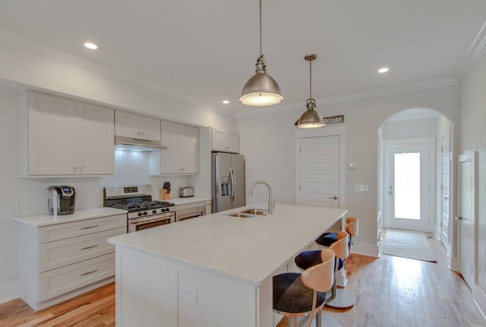 An open kitchen with white cabinetry and stainless appliances flows into the main living area.