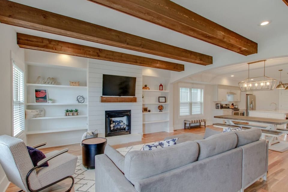 A wide living room view shows the beamed ceilings, couch, and cozy fireplace in full.