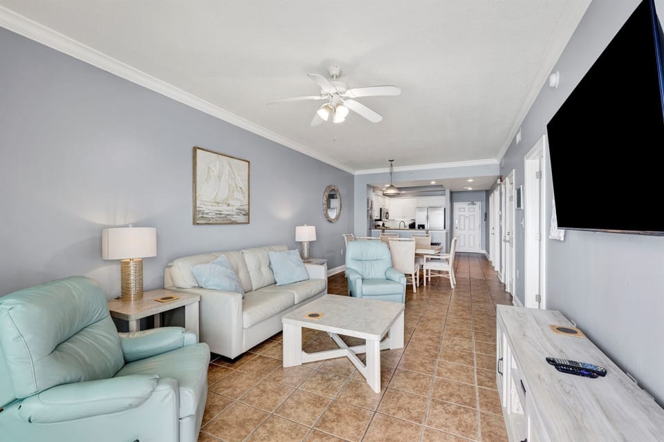 Living area features sliding glass doors leading to balcony, leather sleeper sofa, 2 leather recliners and a wall mounted Smart TV 