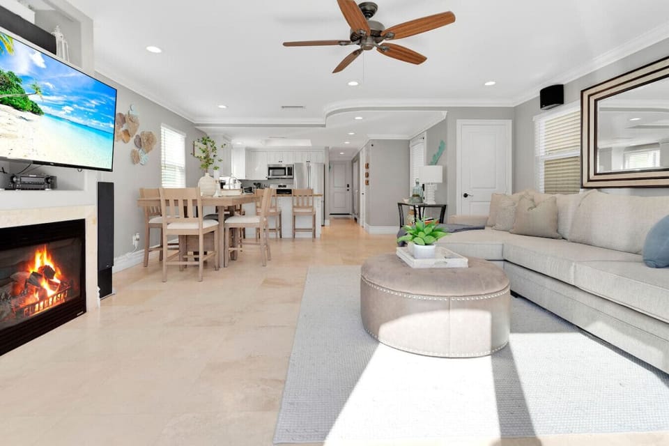 Open-Concept Living Area: Relax by the cozy gas fireplace for movie nights in this open-concept layout featuring a wall-mounted smart TV, deep sectional sofa, custom ceiling fan, and seamless flow into the adjacent dining area and kitchen.