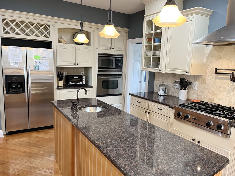 Granite island counter ideal for serving buffet style. Stainless steel fridge.