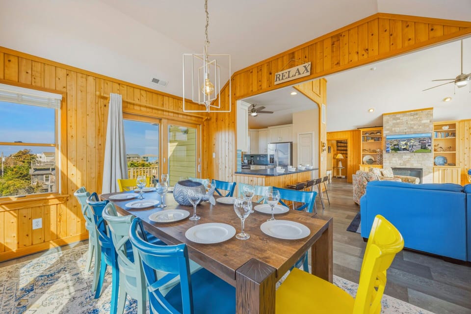 Step into your warm, wood-paneled dining space where colorful chairs invite memorable meals and ocean views create the perfect backdrop for relaxation.