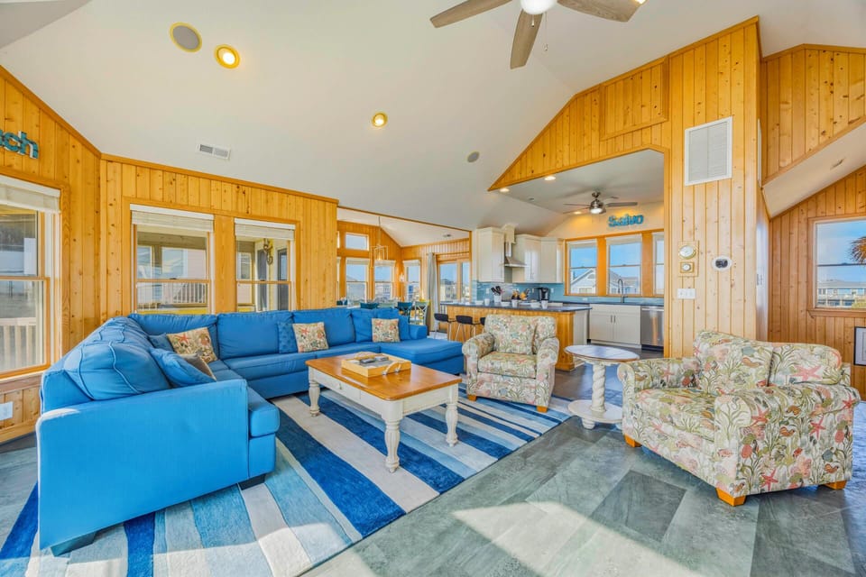 Relax in your spacious living room with plush blue sectional seating and warm wood-paneled walls creating the perfect coastal retreat.