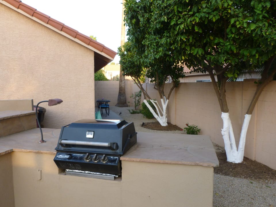 Gas BBQ with view of citrus trees and second patio in the distance.