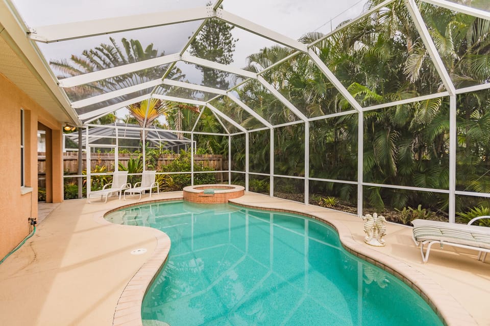 Free form swimming pool with spa and fully enclosed cage and lush landscaping