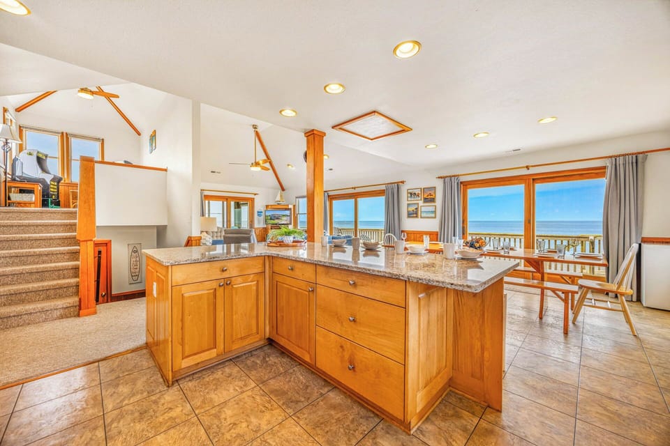 Open your mornings in this sunlit kitchen with stunning ocean views. The granite island and warm wood cabinetry set the stage for coastal cooking, while expansive windows frame endless blue horizons.