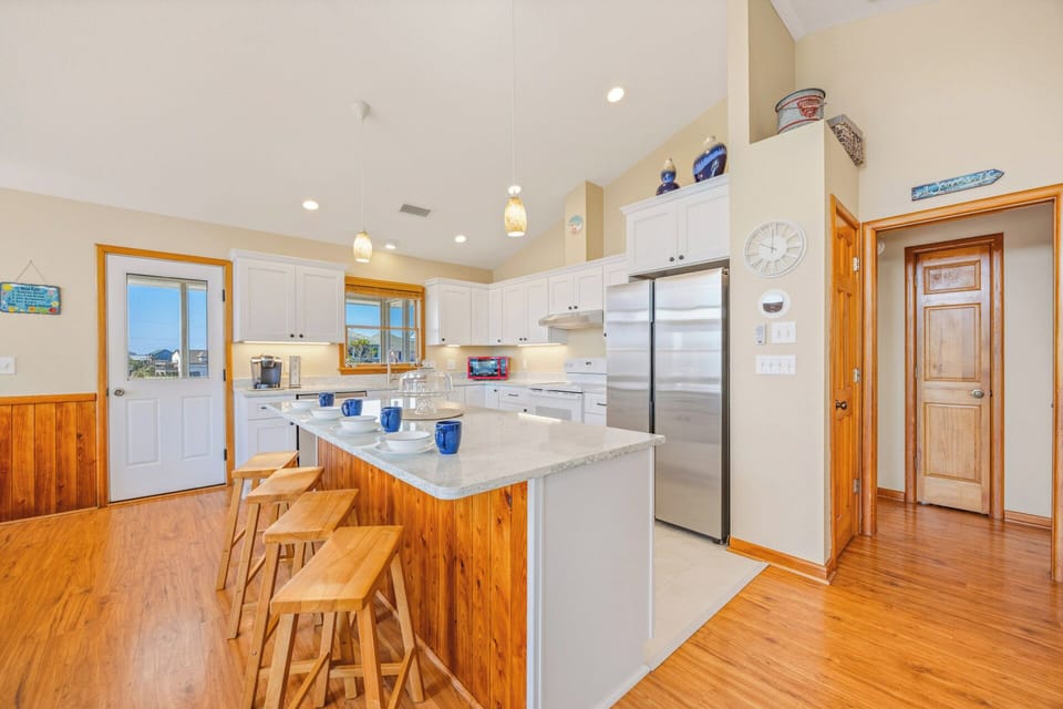 Gather with loved ones in your bright, fully-equipped kitchen featuring vaulted ceilings, marble countertops, and a spacious island perfect for preparing meals and coastal conversations.
