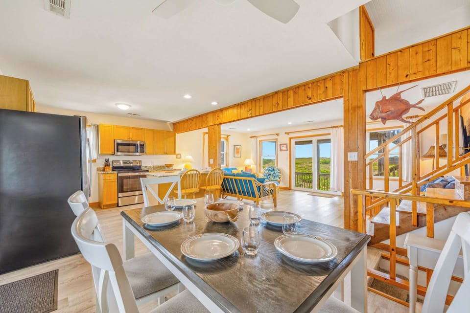 An open-concept living space with warm wood accents and natural light welcomes you home. The full kitchen and dining area flow into a cozy living room, offering serene views and relaxed coastal vibes.