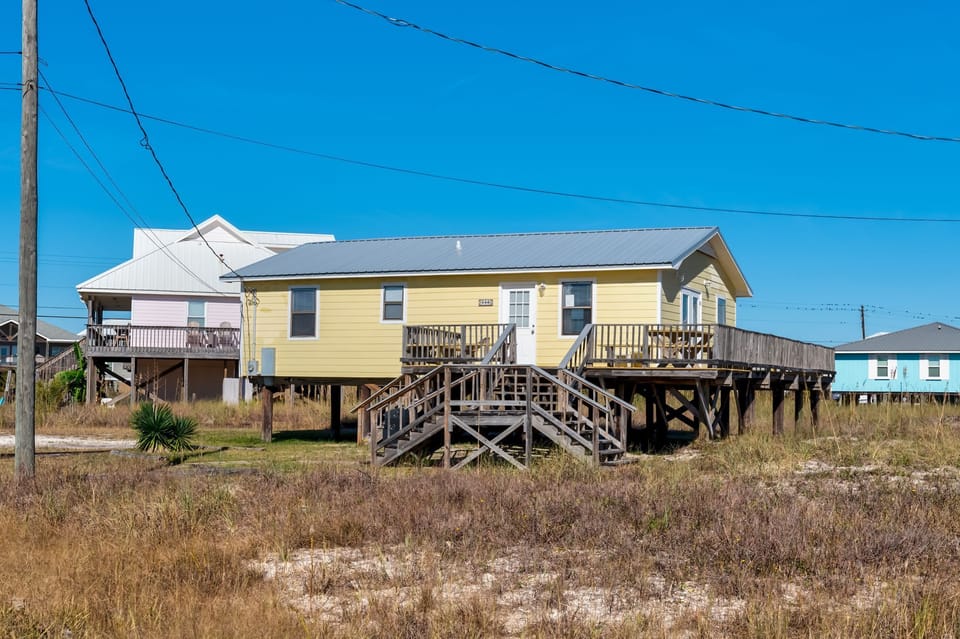 Charming beachside rental with elevated deck surrounded by coastal dunes and natural vegetation.