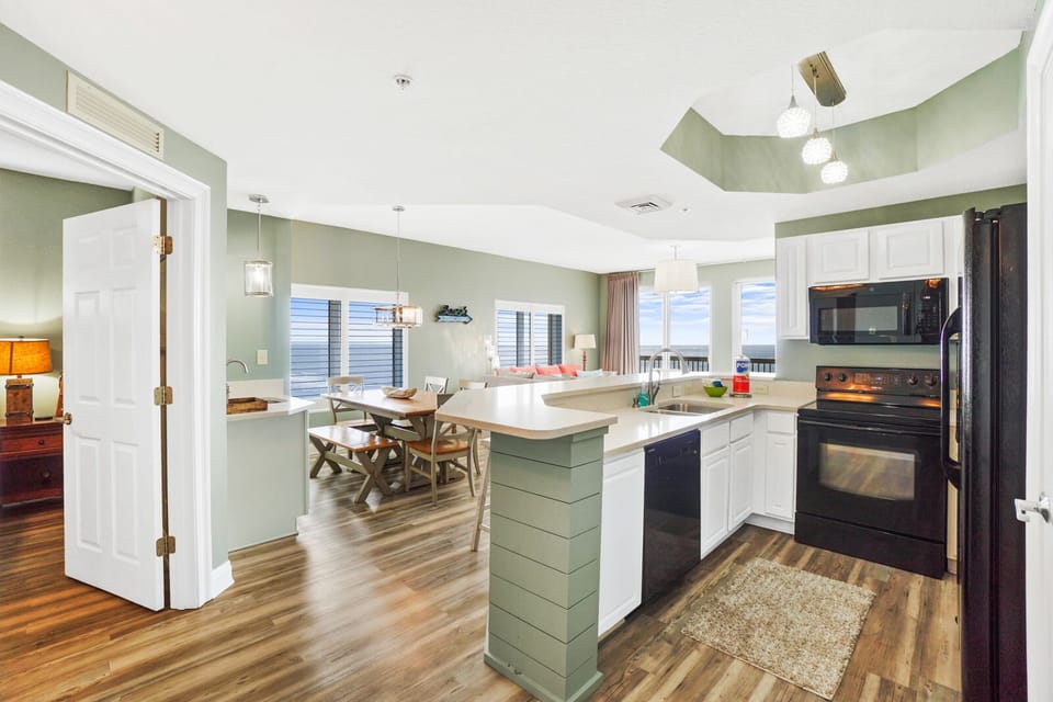 Step into your open-concept haven where coastal green hues and white cabinetry create the perfect space for preparing meals and gathering together.