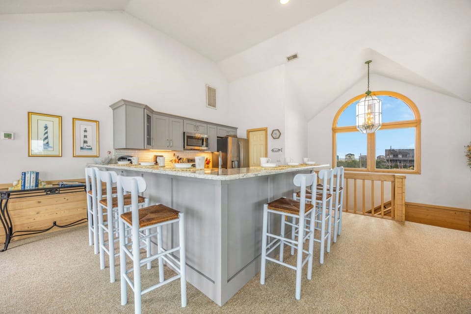 Your open kitchen invites gathering with soaring vaulted ceilings, granite countertops, and bright coastal touches. The arched window frames peaceful views, perfect for morning coffee.