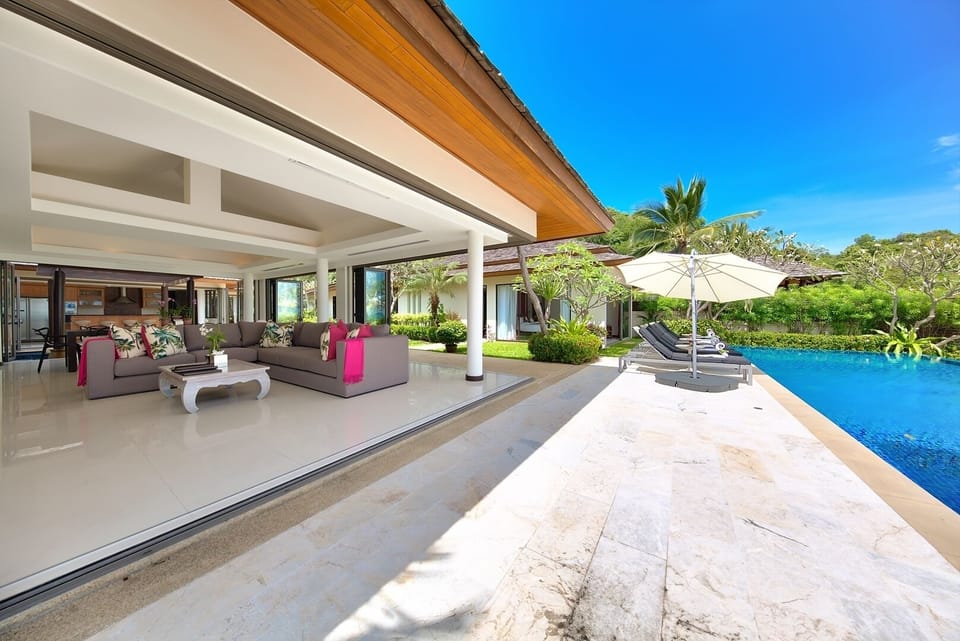 An open air living area with L-shaped sofa, air conditioning & ceiling fan.