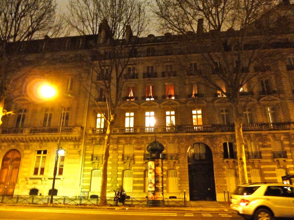 The outside of apartment building at night. Third floor-orange drapes.