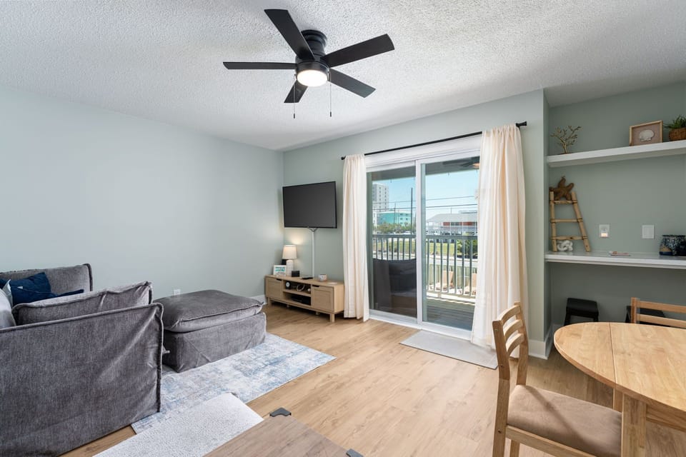Relax in your bright, airy living space with modern ceiling fan, flat-screen TV, and private balcony access overlooking the neighborhood—perfect for unwinding after exploring the city.