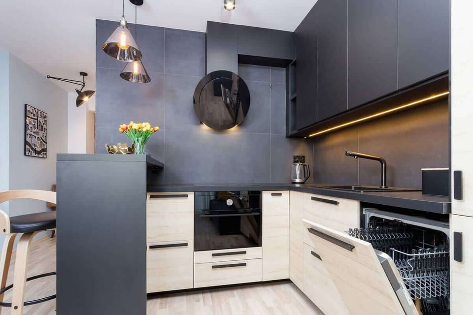 A modern kitchen with black and beige tones, featuring sleek cabinetry and decorative lighting fixtures above the counter.