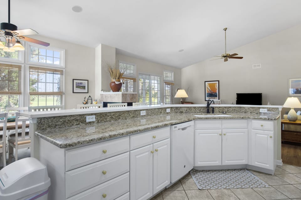 69 Willow Oak Ave - Kitchen Island and Bar Seating - The kitchen features a large, wrap-around breakfast bar with dark granite countertops and white cabinetry. This elevated counter provides a perfect spot for casual meals while looking out into the vaulted great room, maintaining the home's open and social layout.