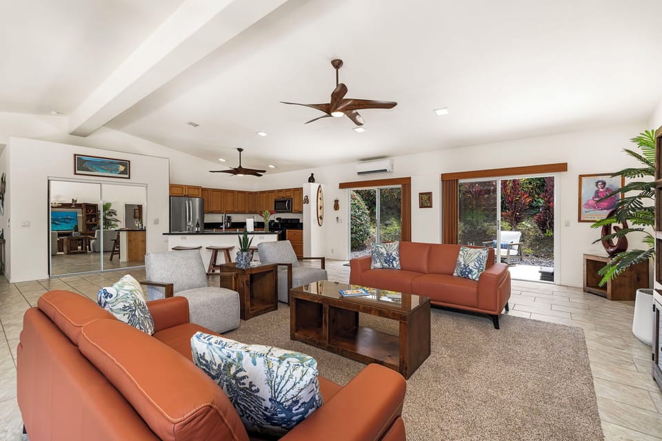 Inviting open-concept space where natural light pours through large windows, ceiling fans cool the air, and vibrant tropical greenery brings the outdoors in.