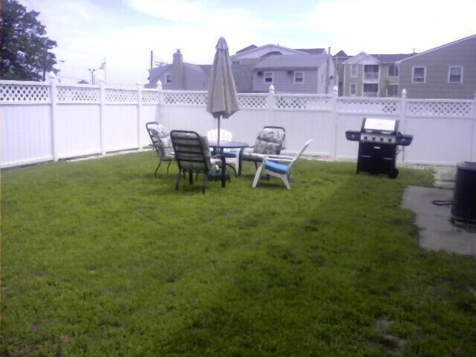 Large, enclosed backyard with chairs, table & grill. 