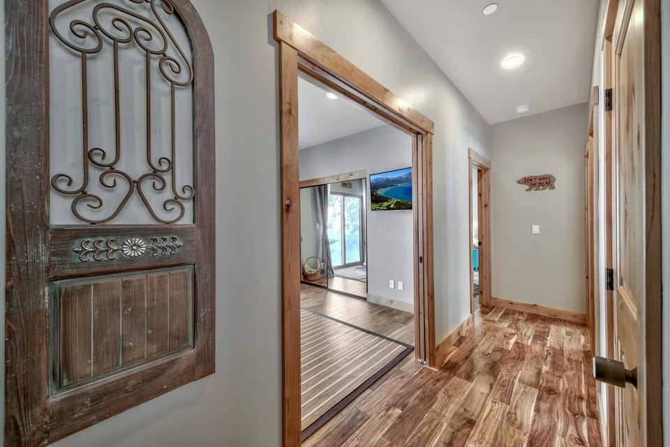 Hallway with glossy wood floors, natural wood trim, and a decorative wrought-iron wall panel near bedroom entrances.