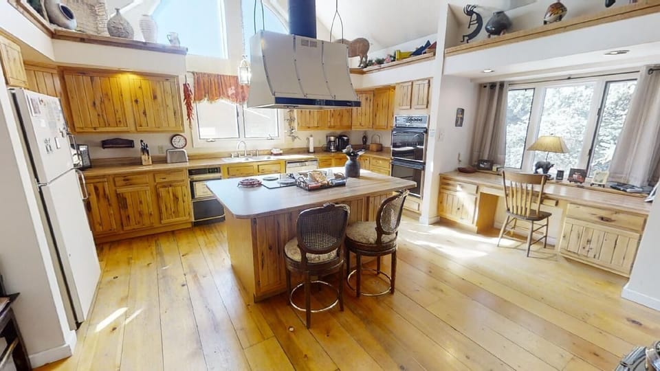 Picture yourself preparing meals in this bright, open kitchen with custom wood cabinetry, a spacious island, and warm natural light streaming through large windows overlooking the peaceful outdoors.