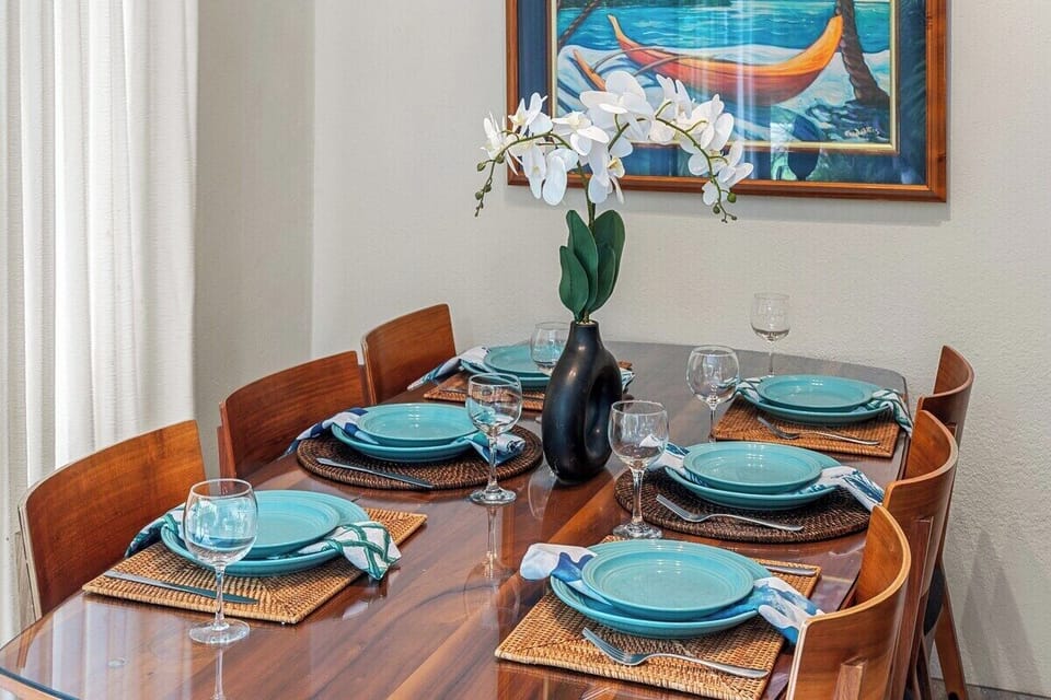 Wooden table set with turquoise plates and orchids, dining framed by art and light.