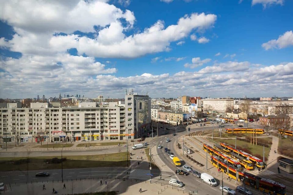 Another balcony view, this time showcasing a wider perspective of the surroundings. The image includes city buildings and the neighborhood environment under a blue sky.