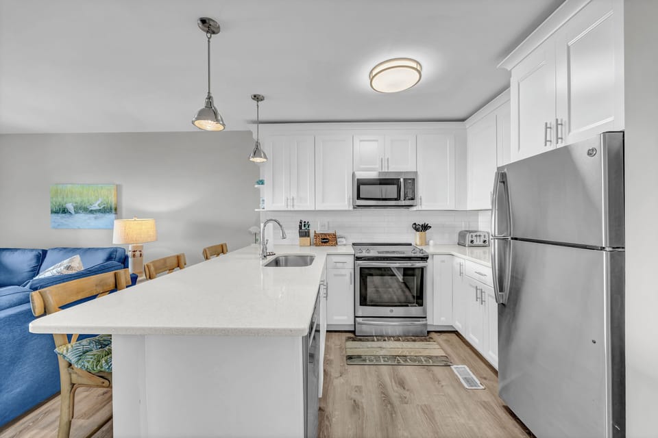 Your fully equipped kitchen awaits with sleek white cabinetry, stainless steel appliances, and a spacious island perfect for meal prep or morning coffee.