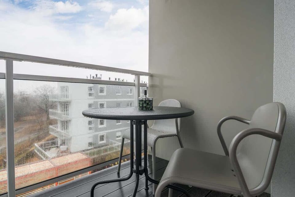 A small balcony with glass railings and a view of nearby buildings, providing a cozy outdoor space for relaxation.