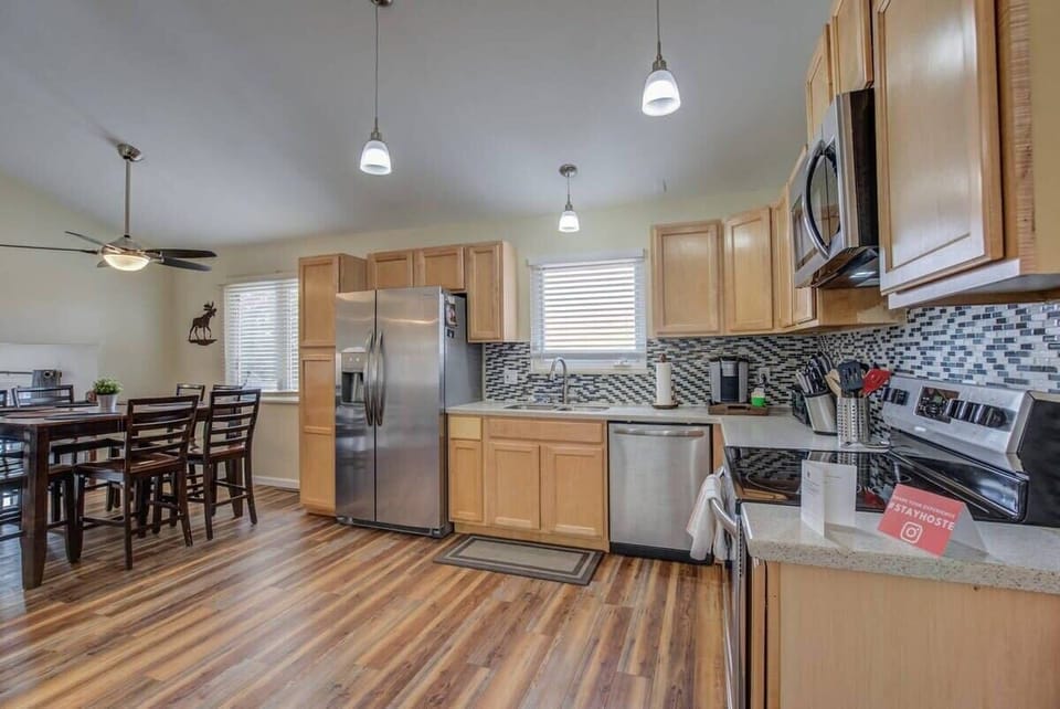 Bright kitchen with light wood cabinets, stainless steel appliances, and a nearby dining table under pendant lights—perfect for cooking a meal, setting out snacks on the counter, and sitting down together to enjoy it.