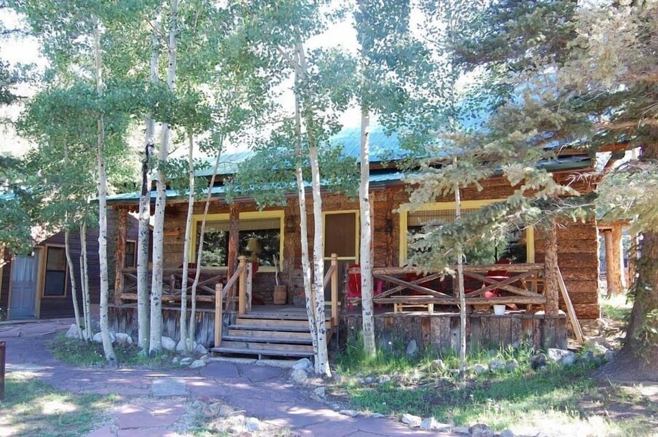 This property is nestled among mature aspen and evergreen trees in a natural mountain setting, offering a secluded atmosphere with rustic exterior charm and a covered outdoor deck perfect for enjoying the alpine scenery.