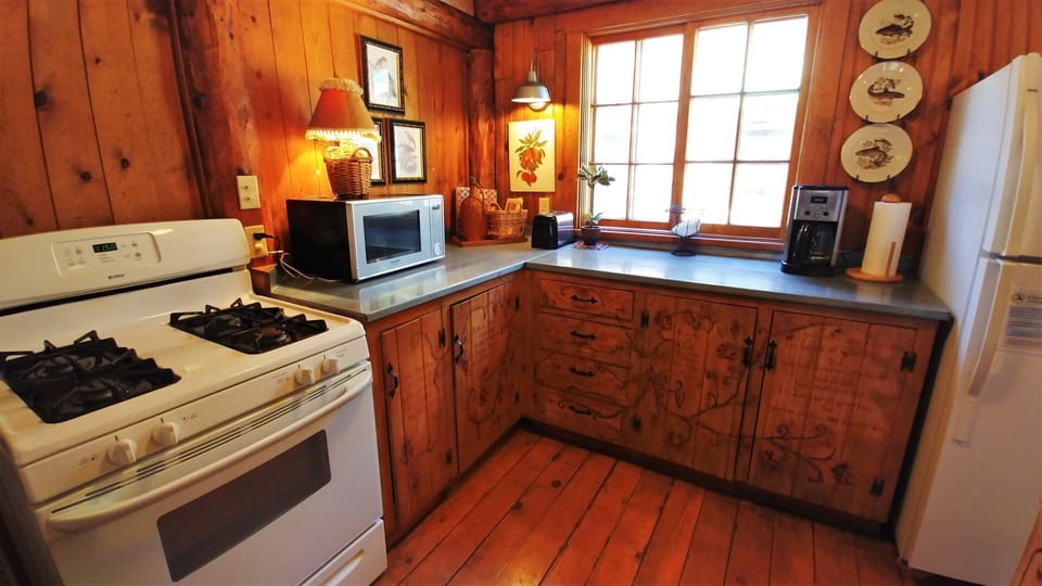 Step into this cozy cabin kitchen where warm wood tones create a rustic retreat. You'll find everything you need with a full stove, microwave, and fridge ready for your culinary adventures.