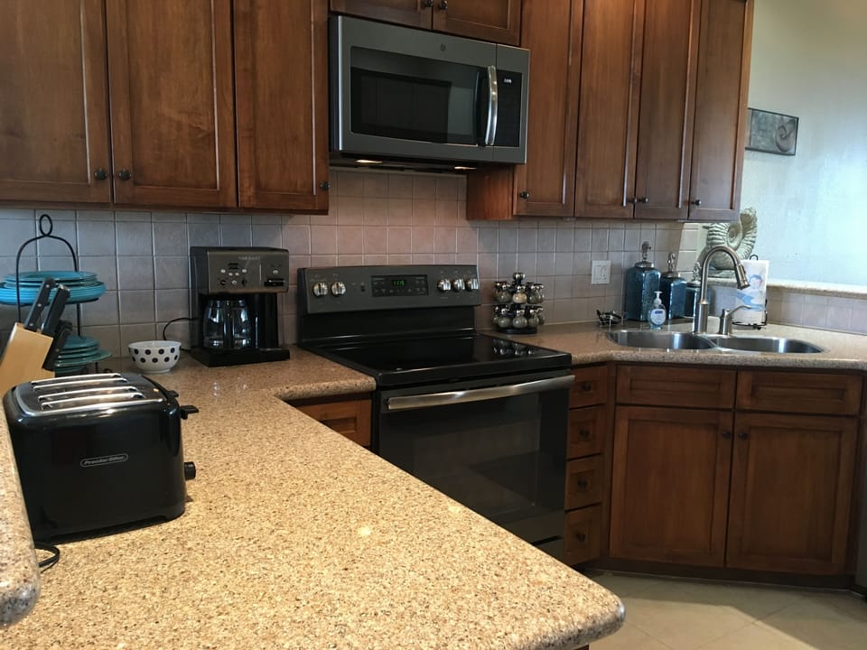 Kitchen equipped with dishwasher, microwave, oven, fridge, blender, coffee pot.
