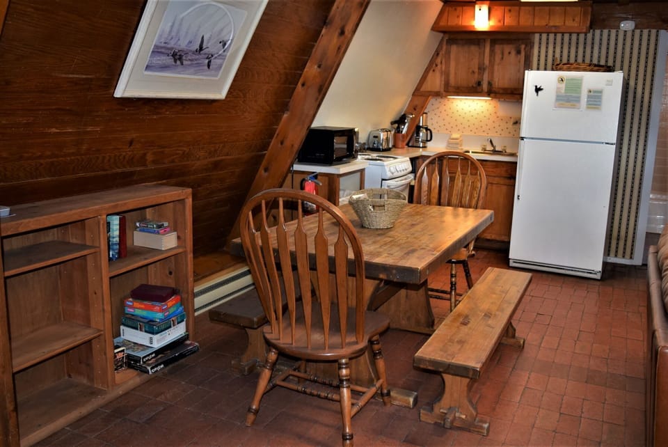 Cozy A-frame retreat with a full kitchen, rustic wooden table, and charming skylight—perfect for preparing meals and gathering with loved ones in a warm, cabin-style setting.