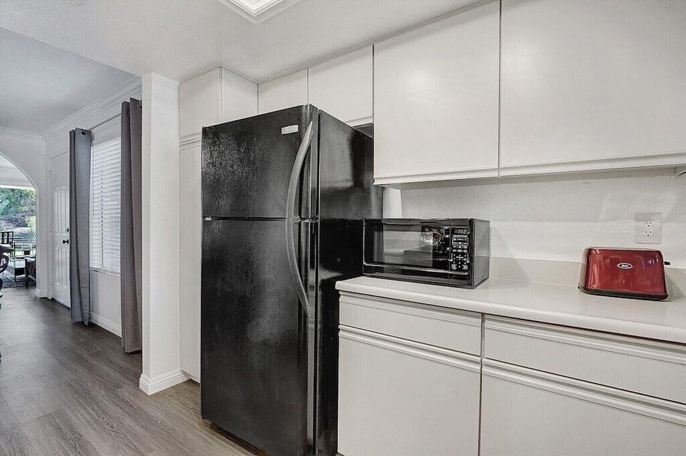- Kitchen with black fridge, microwave, and bright white cabinetry for contrast   - Functional setup with all essentials for a comfortable stay   - Convenient access to dining area and outdoor patio for easy serving
