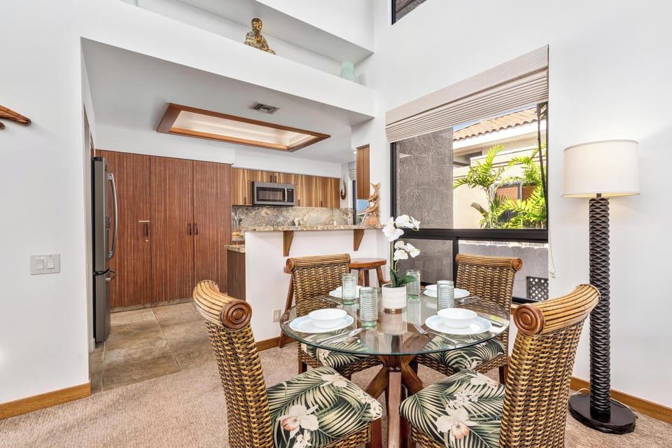 Savor meals in your elegant dining space, where tropical-print chairs surround a glass table beneath warm wood accents and natural light.