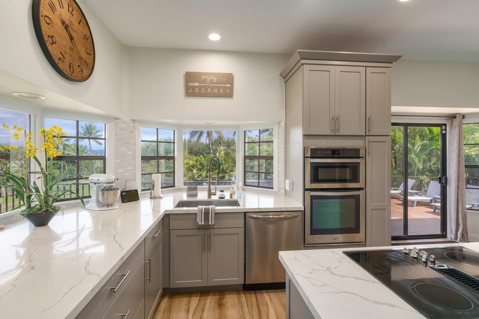 This bright kitchen features a corner window overlooking tropical gardens and palm trees, creating a peaceful ambiance while cooking.