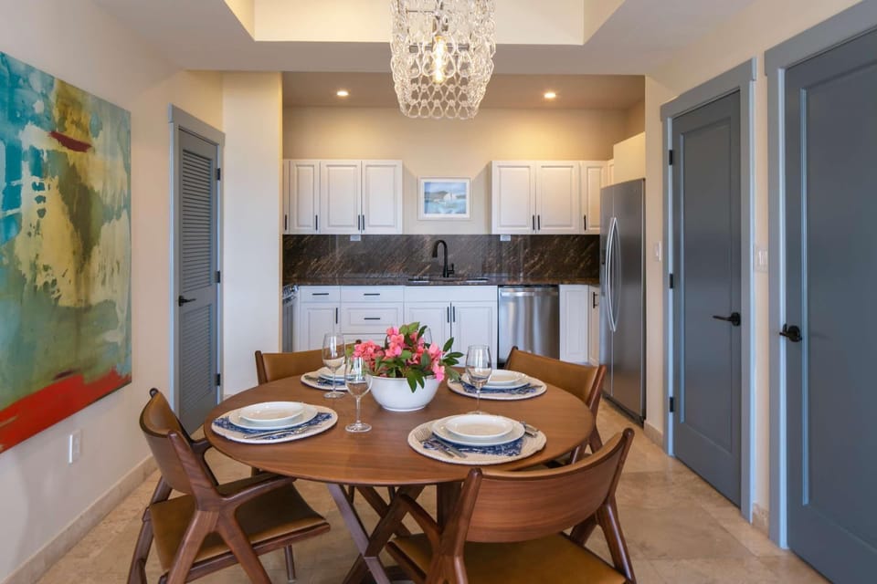 Round wood dining table set with white dishes and pink flowers sits before white cabinetry and stainless steel appliances.