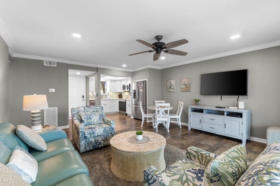 Relax in your coastal-inspired living space with soft blue furnishings, open kitchen, and entertainment setup for perfect vacation downtime.