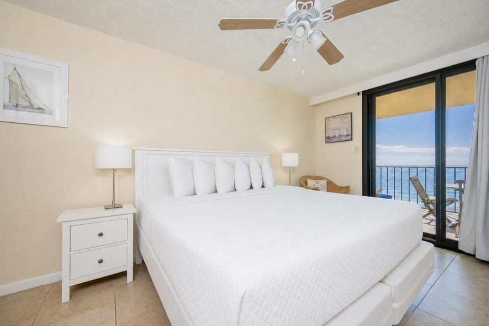 Bright master bedroom featuring a king bed, bedside lamp, and the balcony with seating overlooking the tranquil beachfront