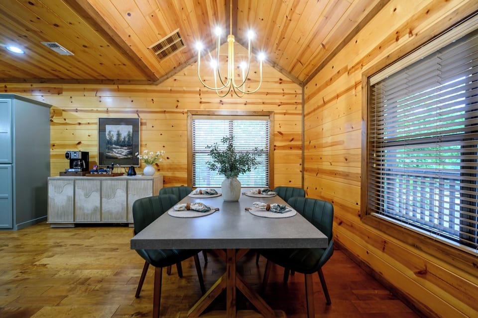 Gather around the elegant dining table beneath vaulted wood ceilings, where natural light streams through large windows. The stylish modern furnishings and warm cabin ambiance create the perfect setting for your memorable meals together.