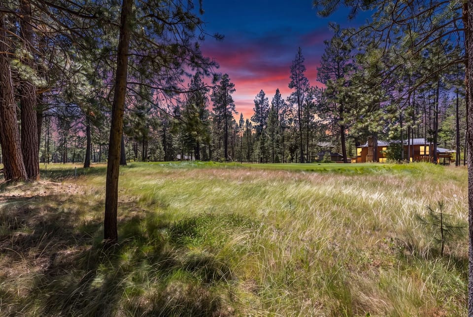 A stunning sunset paints the sky in vibrant pinks and purples over the property, nestled among towering pines and a peaceful meadow.