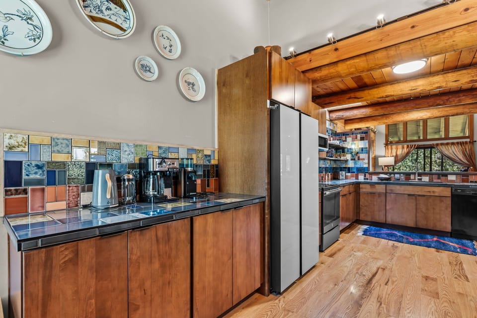 Cook meals in this charming, fully equipped kitchen with rustic wood beams, colorful tile backsplash, and modern appliances. The cozy details and warm atmosphere make preparing breakfast together a delight.