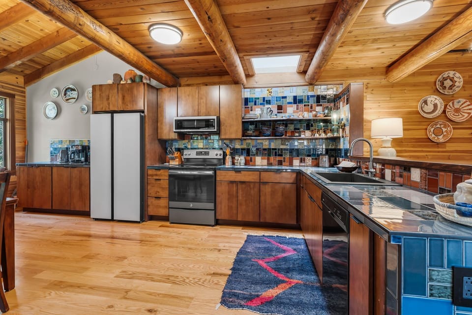 Your spacious kitchen features warm wooden cabinets, colorful tiled backsplash, and modern appliances beneath stunning exposed beam ceilings—perfect for preparing memorable meals during your mountain getaway.