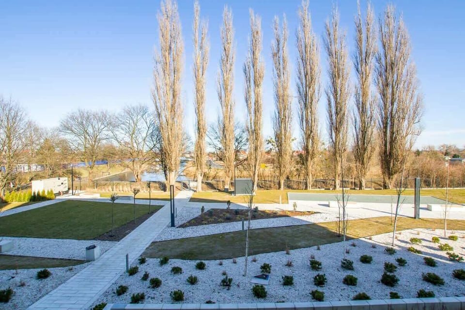 A landscape view from the balcony, overlooking a neatly maintained garden area with tall trees and structured walkways.