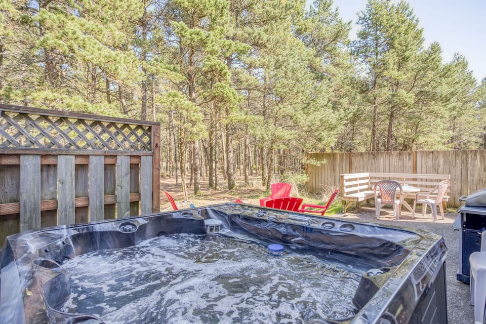 Soak your cares away in the private hot tub, surrounded by towering pines and cozy seating—your perfect retreat under the open sky.