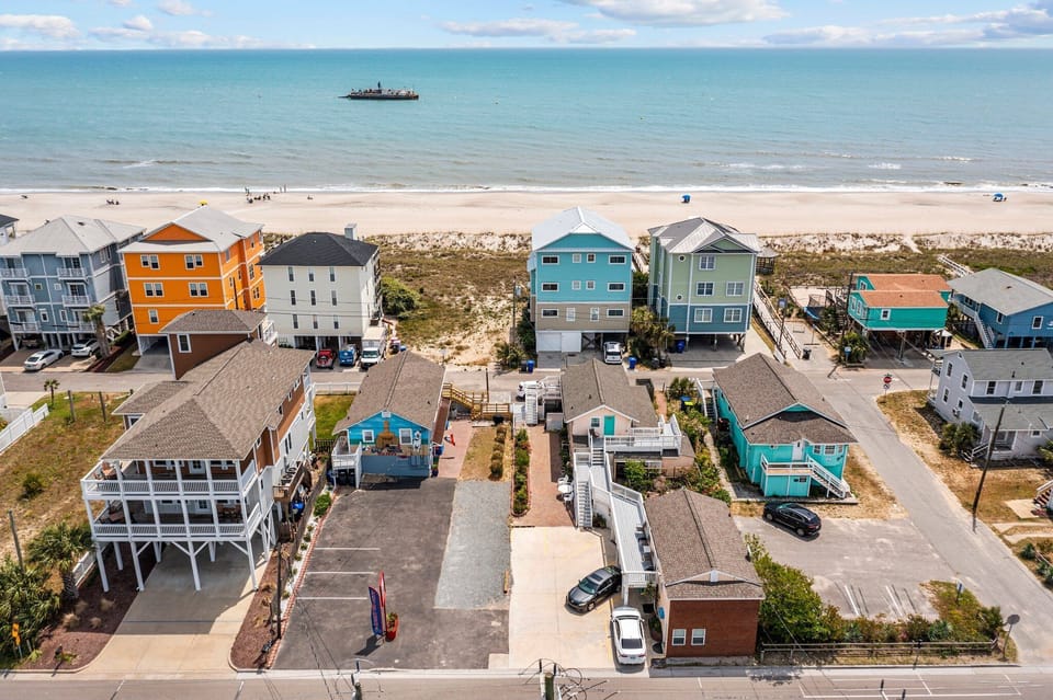 Colorful beachfront vacation homes line the sandy shore, offering direct beach access and stunning ocean views with a boat visible offshore.