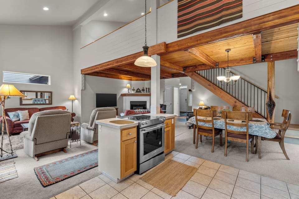 Step into your open-concept retreat where vaulted wood-beam ceilings soar overhead, creating a warm and inviting great room with modern kitchen, cozy living space, and dining for your group.