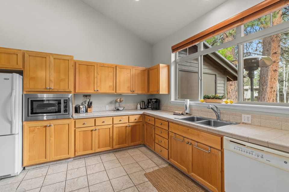 Cook up your favorite meals in this bright, fully-equipped kitchen with warm wood cabinetry, modern appliances, and peaceful forest views through expansive windows.