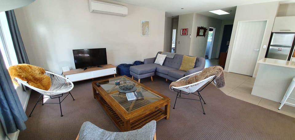 Open plan living room with comfy chairs and sofa, flat screen TV, and heat pump